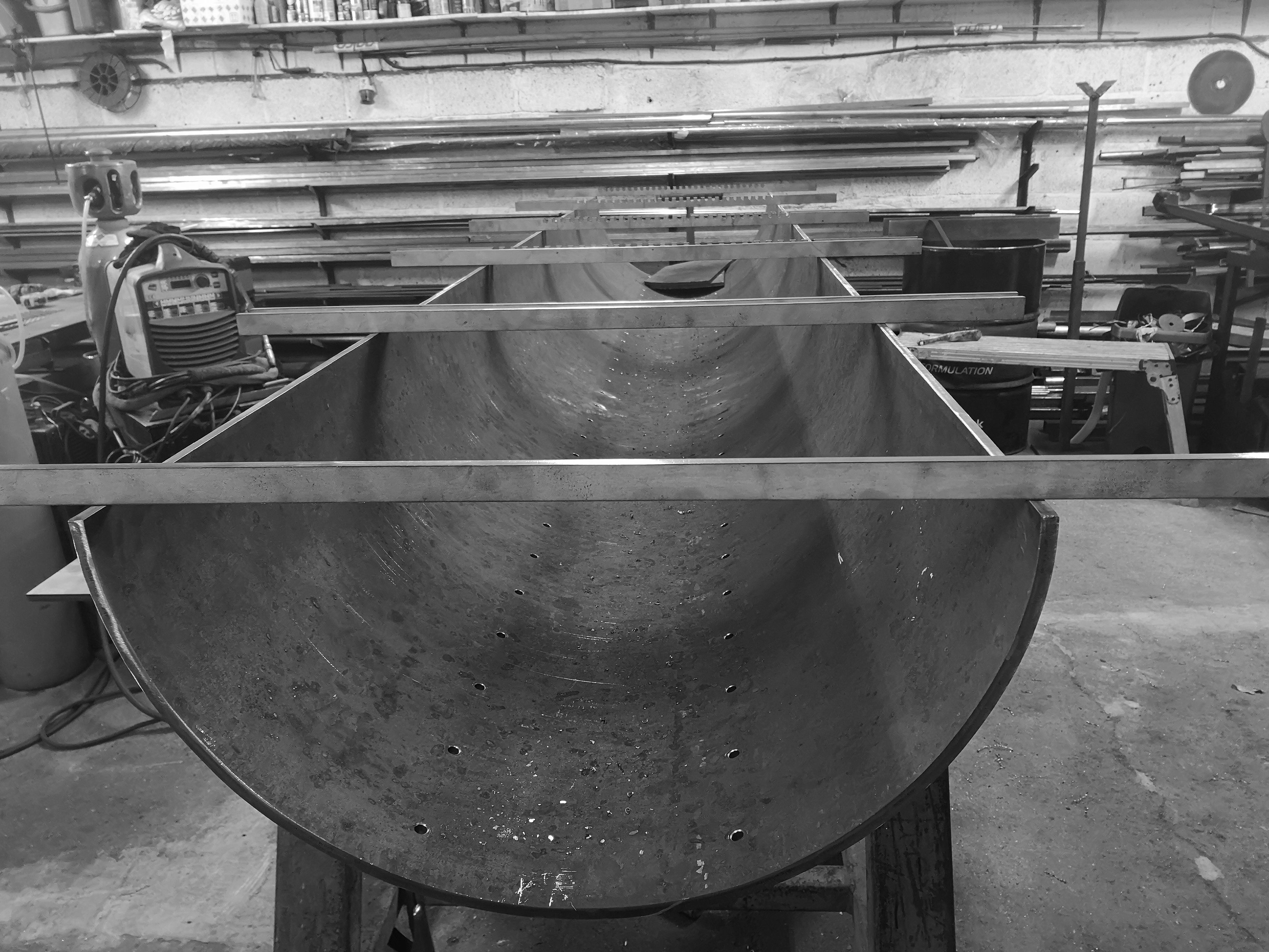 Black and white image of a firepit being constructed in a fabrication workshop.